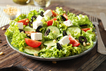 Plate with tasty greek salad of fresh vegetables on wooden background