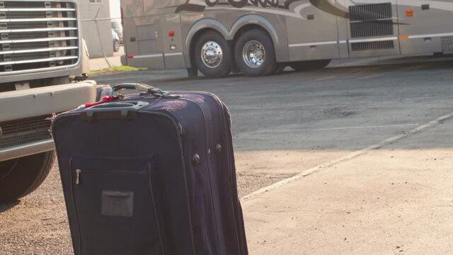 A piece of luggage left on the tarmac of a bus stop and a crowd of people walk by it.