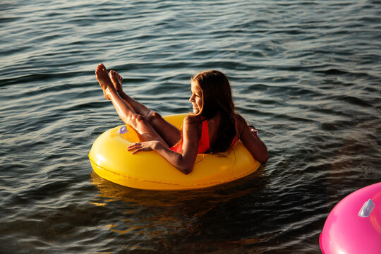 The child floating on water in a large inflatable circle. Young firl raised legs up and prefer swimming relaxation