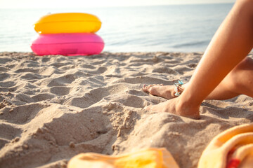 Cropped photo of the leg of tan girl relax on the beach and take sunbath on summer vacation. child sit on the towel on the sand beach and eat the fruit at the background sea and rubber ring