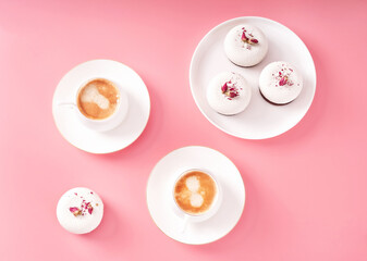 Mousse pastry dessert covered with white chocolate decorated with rose buds and two porcelain cups of coffee on pastel pink background. Modern stylish cake. Flat lay style. Copy space. Close-up.