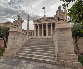 Naklejka premium Plato and Socrates statues in front of the national academy of Athens Greece under impressive cloudy sky, filtered image