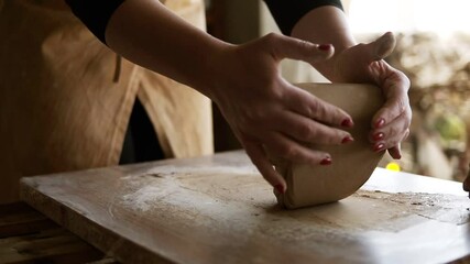 Close up footage of female hands with beautiful red manicure holding clay and kneading it on a worktop. Wearing beige apron. Unrecognizable person. Soft clay - Powered by Adobe