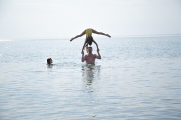Father take fun with his daughters. The kids do acrobat element in water on the water