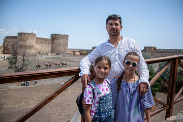 Happy father posing to the camera with two preteen daughter wo sisters together on travel vacation  in historic place fortress.