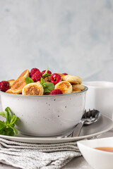 Bowl with tiny pancake cereal with raspberries, mint and jam on a light grey concrete background. Trendy food. Mini cereal pancakes. Pancake porridge.
