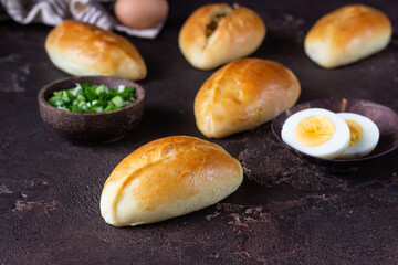 Traditional Russian pies with green onion and egg on wooden plate, dark rustic background. Russian pirozhki, homemade baked patties.