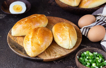 Traditional Russian pies with green onion and egg on wooden plate, dark rustic background. Russian pirozhki, homemade baked patties.