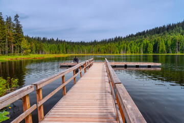 Naklejka premium fisherman with a fishing rod catches fish in the lake, sitting on a chair on the platform of a wooden dock