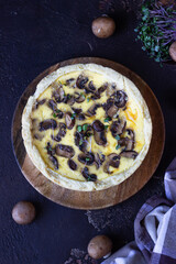 Savory tart, pie or quiche with mushrooms and cheese on wooden plate, dark brown textured background. Homemade savory autumn bakery. Top view.