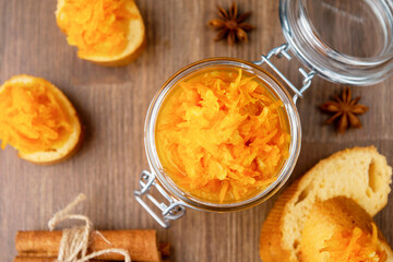 A jar of orange confiture with pieces of French baguette, cinnamon and star anise on the wooden background,