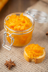 A jar of orange confiture and pieces of French baguette with star anise on the sackcloth and wooden background
