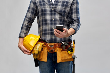 repair, construction and building - male worker or builder with smartphone and working tools on belt over grey background