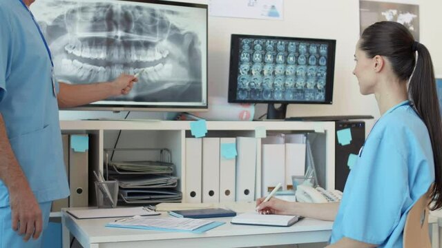 Lockdown of unrecognizable male prosthodontist teaching young female intern how to analyze x-ray image of teeth. Then woman looking at camera and smiling