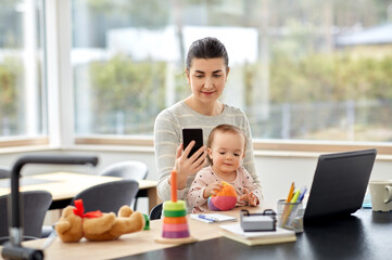 remote job, multi-tasking and family concept - happy smiling mother with baby, smartphone and laptop working at home office