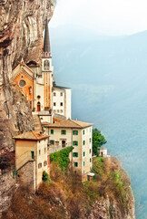 Naklejka premium Stone steps of stairs to Ancient Madonna della Corona santuario facade under rocks in high mountains, Veneto region, Italy, famous touristic landmark.