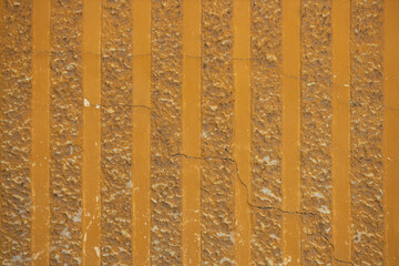 Decorative parget texture background. Wall fragment with vertical striped pattern. Structural plaster, rough, uneven surface in orange yellow color.