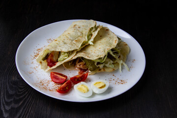 Sliced ​​chicken with canned  cucumbers and cabbage in sauce, wrapped in pita bread on a white plate. Delicious for lunch or dinner. Pieces of tomato and eggs on a plate with pita bread