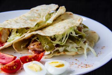 Sliced ​​chicken with canned  cucumbers and cabbage in sauce, wrapped in pita bread on a white plate. Delicious for lunch or dinner. Pieces of tomato and eggs on a plate with pita bread