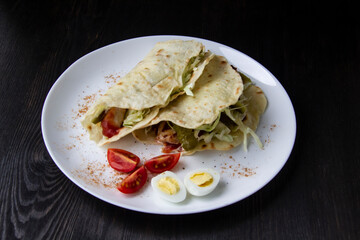 Sliced ​​chicken with canned  cucumbers and cabbage in sauce, wrapped in pita bread on a white plate. Delicious for lunch or dinner. Pieces of tomato and eggs on a plate with pita bread