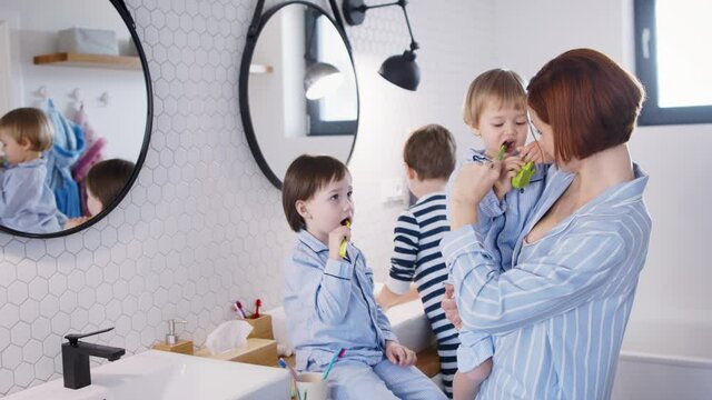 Mother with small children in pajamas in bathroom at home, brushing teeth.