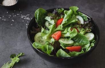vegetable salad of fresh tomato, cucumber, cos, green and red oak lettuce ,sesame and sunflower sprouts on black bowl. Diet and vegetarian menu. concept for a tasty and healthy meal.