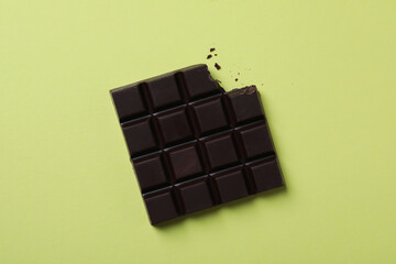 Tasty dark chocolate bar with bite mark on yellow background, top view