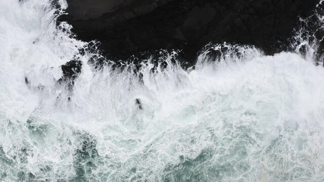 Aerial top down view of foamy waves smashing onto rocks.