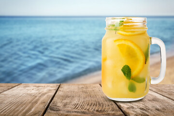 Mason jar with lemonade on wooden table near sea, space for text