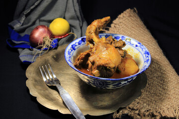 Boiled chicken Curry into white pot. Hot and spicy Chicken Curry with green lemon & chili, onion isolated on black background.
