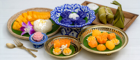 Thai traditional dessert serving on porcelain, wooden tray and brass tray with brass cutlery on plank table
