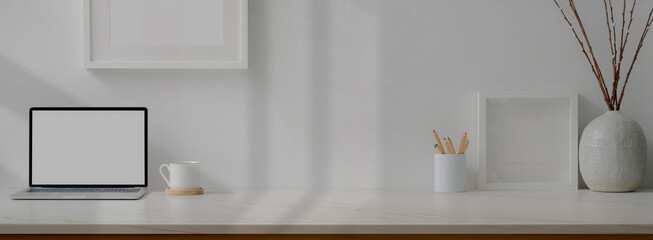 Minimal home office desk with mock-up laptop, cup, stationery, decorations and copy space on marble table