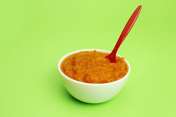 pumpkin porridge in a bowl with a spoon on a green background, baby or vegan food. Copy space
