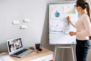 Online business coach conducts webinar online. Young confident woman writes on flip chart with...