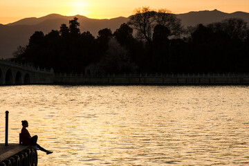Silhouette of a woman sitting on a pier at sunset, Beijing, China