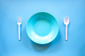 Blue plasstic plate with white plasstic spoon and fork on blue background