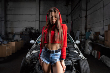 Fototapeta na wymiar Portrait woman in jeans shorts and top posing next to a car in the garage, in background old car Creative Colorful Bright neon Portrait .Design Car workshop art concept