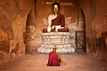 Buddhist monk sitting and praying in front of Buddha statue in ancient town of Bagan, Myanmar (Burma) 