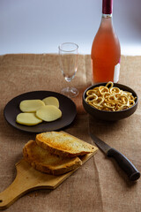 still life con aperitivo con pan tostado, queso, salados y vino rosado sobre mantel rustico