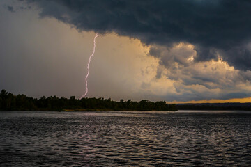 Naklejka na ściany i meble Lightning strike over the river, stormy weather, dark clouds in the sky, beginning of thunderstorm, photo was taken in Ukraine