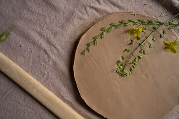 Top view of a plants lying on the clay piece while being used for creation of a special ornament on it. Creative process. Work with rolling pin.