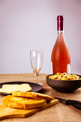 still life con aperitivo con pan tostado, queso, salados y vino rosado sobre mantel rustico