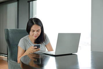 Young beautiful asian woman using smartphone and laptop computer working online at home and feel...