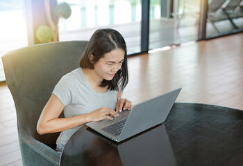 Beautiful asian woman in casual dress using laptop computer working online at home with looking...