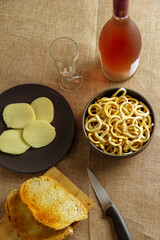 still life con aperitivo con pan tostado, queso, salados y vino rosado sobre mantel rustico