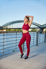 Fit in the city, young woman doing gymnastics and stretching exercises on the river early in the morning after sunrise