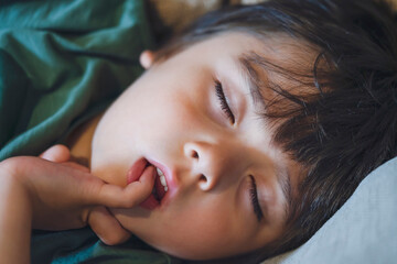 Close up face kid sleeping on sofa, Candid shot Child puting finger in his mounth while sleeping, Tired boy taking a nap in the afternoon spring or summer, Mental health Children concept