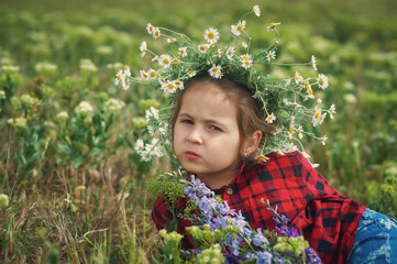 Portrait of a little girl in a field with a wreath of daisies . Children's outdoor walks
