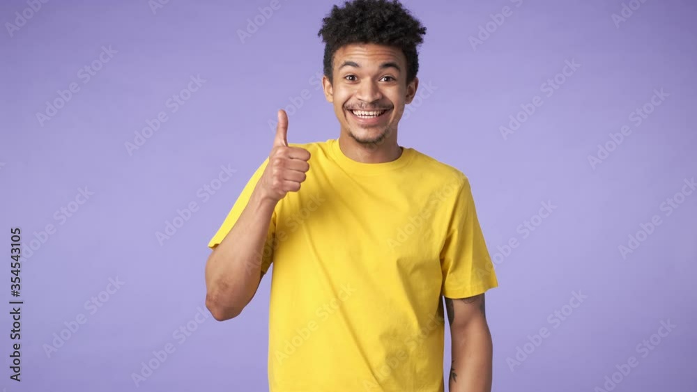 Sticker Young happy cheery african guy isolated over purple background showing thumbs up gesture