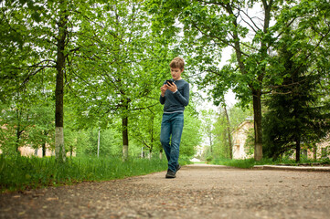 A teenager is walking in the park with a phone in his hand.